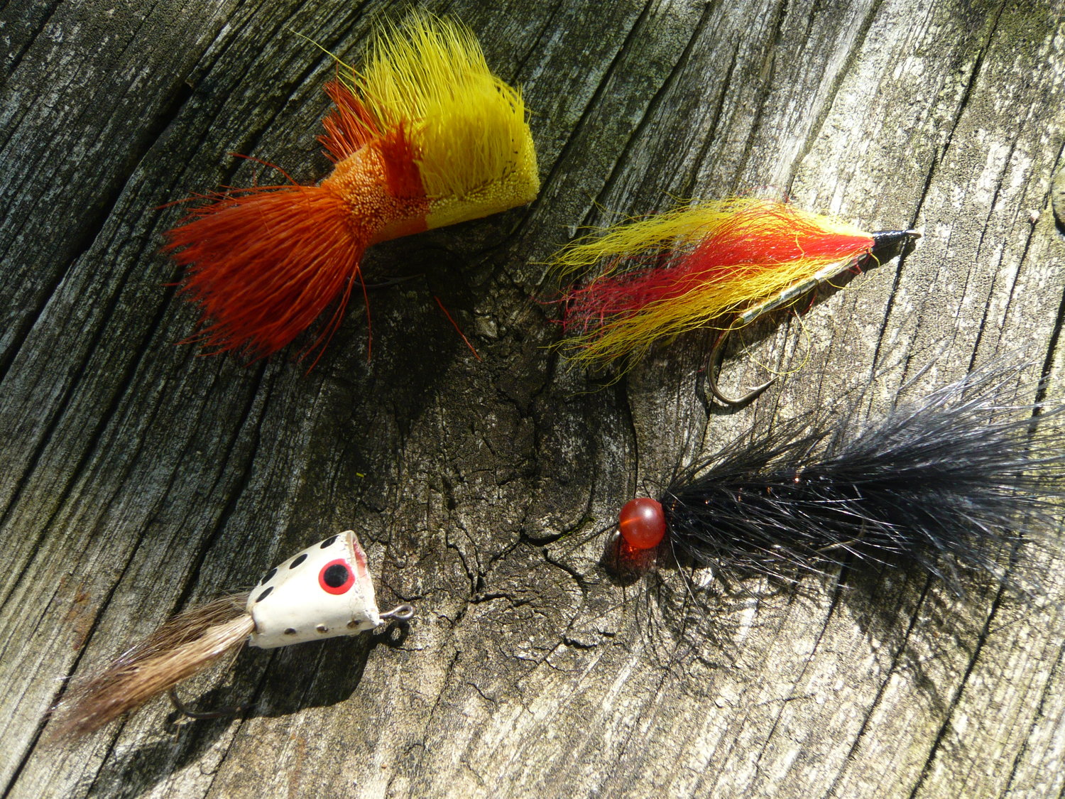 Clockwise from lower left: A popper, deer hair bug, streamer fly and black woolly bugger. The types of large flies used for bass with a fly rod.